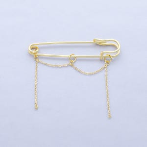 May include: A gold safety pin with three dangling chains. The chains are connected to the pin at the top and bottom.