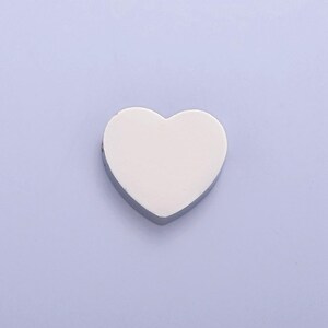 Puede incluir: Un charm de coraz&oacute;n plateado con una superficie lisa y blanca. El charm es perfecto para agregar un toque de amor a los proyectos de joyer&iacute;a.