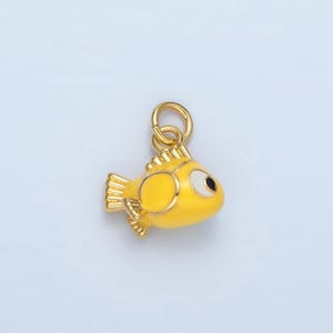 May include: A gold-colored charm shaped like a yellow fish with a white eye and black pupil. The charm has a loop at the top for attaching to a bracelet or necklace.