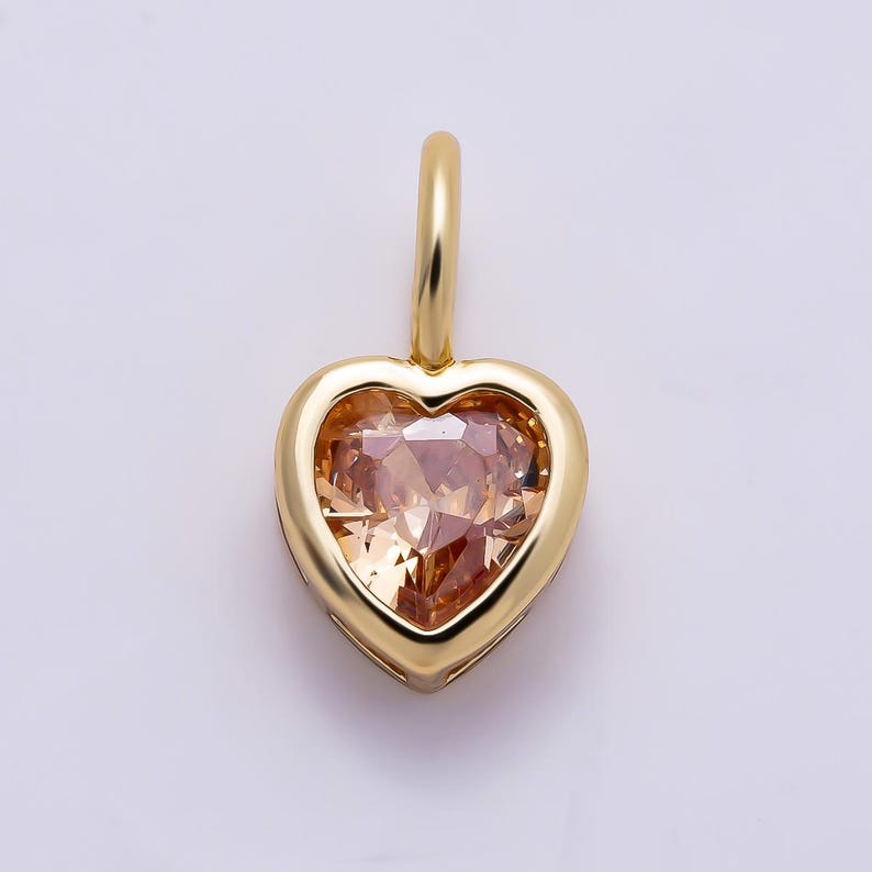 May include: A heart-shaped pendant featuring a faceted, light champagne-colored gemstone set within a polished yellow gold frame. The pendant includes a small, smooth yellow gold bail at the top for attachment to a chain or necklace.