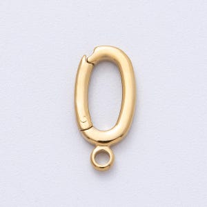 May include: A gold-colored oval-shaped clasp with a spring-loaded closure. The clasp has a small loop at the bottom for attaching to jewelry or other items. The metal has a polished finish.