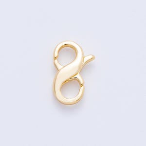 May include: A gold-colored lobster clasp, a jewelry component, is displayed against a white background. The clasp has a curved, elongated shape with a spring-loaded mechanism for secure closure. The metal has a shiny, polished finish.