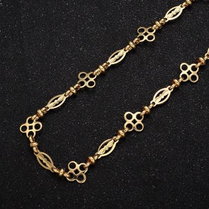 May include: A gold chain necklace with a delicate, intricate design. The chain features a repeating pattern of small, oval-shaped links connected by larger, four-leaf clover-shaped links.