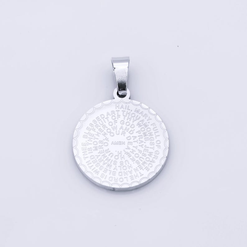 May include: Silver pendant with a circular design featuring the Hail Mary prayer in a spiral pattern.
