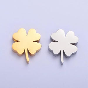 May include: Two four-leaf clover charms, one gold and one silver. The charms are made of metal and have a shiny finish.