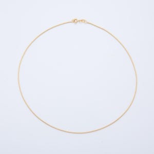 May include: A delicate gold-colored necklace with a simple, elegant design. The necklace is a thin, circular chain with a clasp closure. The chain is smooth and appears to be made of a shiny metal.