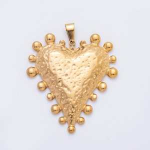Peut inclure: Pendentif en forme de cœur doré, avec une surface texturée et une série de petits ornements ronds sur les bords. Le pendentif a une boucle en haut pour une chaîne. La forme de cœur est proéminente, et le design est orné.