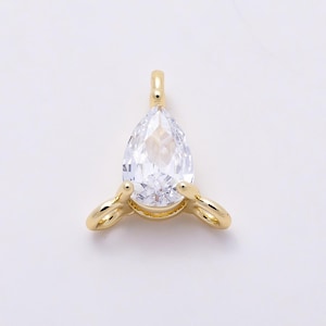 May include: A gold-toned metal pendant featuring a clear, pear-shaped faceted gemstone set in a prong setting. The pendant includes a small vertical loop at the top and two additional horizontal loops extending from the base sides.
