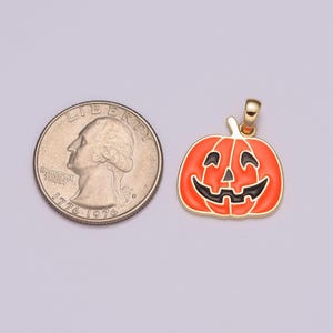 Pu&ograve; includere: Un ciondolo dorato a forma di zucca di Halloween con un viso sorridente. La zucca &egrave; arancione con occhi, naso e bocca neri. Il ciondolo &egrave; accanto a una moneta da un quarto di dollaro americano per il confronto delle dimensioni.
