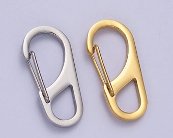 Op de afbeelding: Twee metalen sleutelhangers, een zilveren en een gouden, met een haak en een lus. De sleutelhangers liggen op een witte achtergrond.