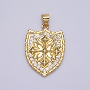 May include: A gold pendant in the shape of a shield with a cross design and clear cubic zirconia stones.