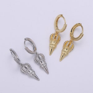 Puede incluir: Un par de pendientes de aro dorados y plateados con un diseño de corona y calavera. Los pendientes están hechos de metal y tienen un colgante.