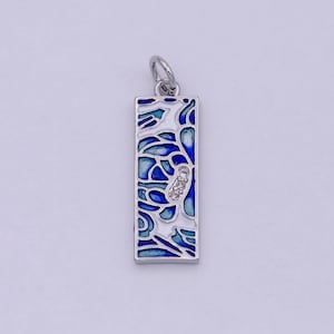 Könnte beinhalten: Ein silberner Anhänger mit einem blauen und weißen Emaille-Design. Der Anhänger ist rechteckig und hat einen kleinen, klaren Stein in der Mitte.