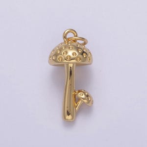 Puede incluir: Un amuleto de champiñón de color dorado con una parte superior texturizada y un tallo pequeño. El amuleto tiene un bucle en la parte superior para sujetarlo a un collar o pulsera.
