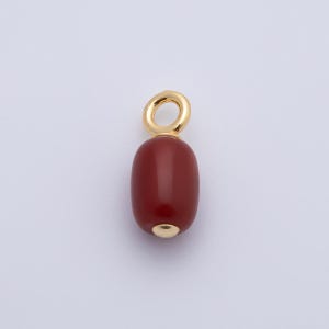 May include: A red-brown, oval-shaped pendant with a gold-colored loop at the top and a gold-colored cap at the bottom. The pendant is smooth and polished, and it hangs against a light background. This jewelry piece is suitable for necklaces or bracelets.