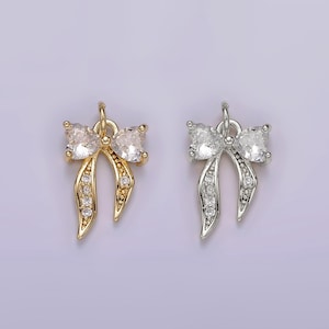 May include: Two bow-shaped charms with clear crystal accents. One charm is gold-toned and the other is silver-toned.