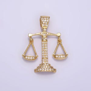 May include: A gold-tone pendant featuring a detailed scale of justice design, fully encrusted with clear sparkling stones.