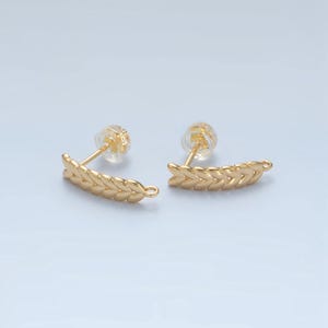 May include: A pair of gold-toned earrings with a leaf design. The earrings are made of a braided pattern of leaves and have a small loop at the end for attaching a charm.