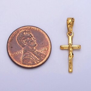 May include: A gold-colored crucifix pendant with a detailed depiction of Jesus Christ. The pendant is shown next to a U.S. penny for size comparison. The penny is dated 2009.