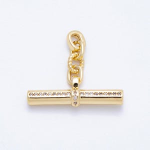 May include: A gold-colored toggle clasp with a T-bar design. The bar is adorned with small, clear crystals. The clasp is connected to a chain with a twisted rope design. The jewelry component is set against a white background.