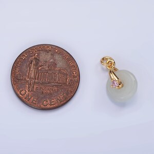 Pu&ograve; includere: Ciondolo in oro con un disco di giada bianca e un cristallo rosa. Il ciondolo &egrave; circa delle dimensioni di una moneta da un centesimo di dollaro americano.