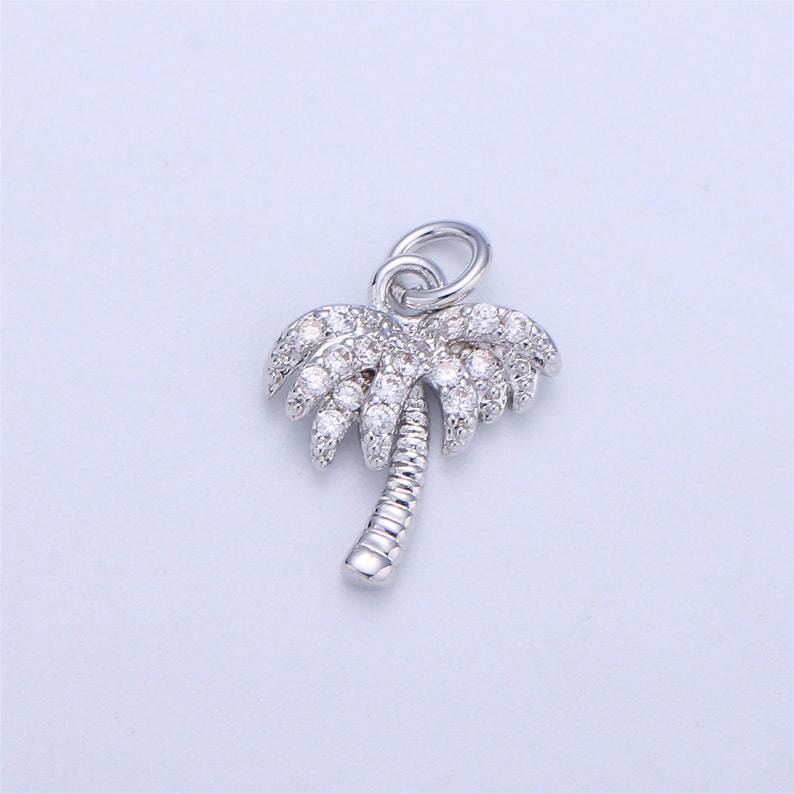 May include: A silver palm tree charm with clear cubic zirconia stones. The charm has a loop at the top for attaching to a bracelet or necklace.