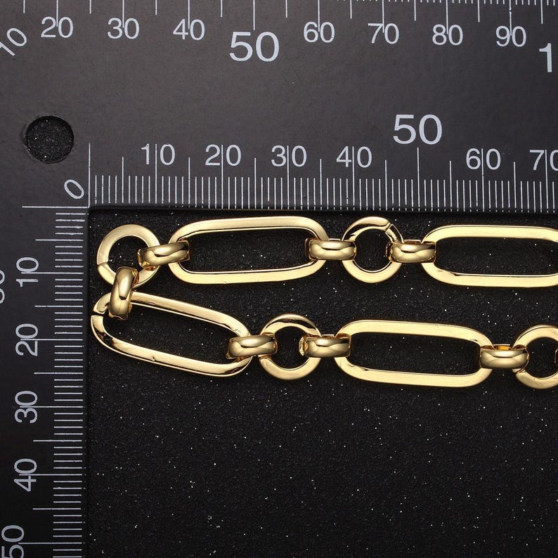 May include: A gold chain necklace with a link style that is oval shaped. The chain is measured against a ruler.