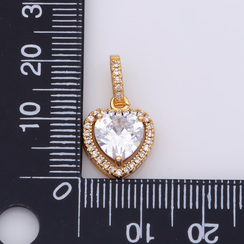 May include: A gold heart-shaped pendant featuring a large clear cubic zirconia stone surrounded by smaller cubic zirconia stones.
