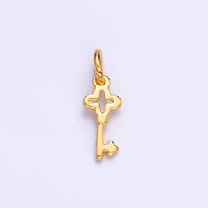 Pode incluir: Um amuleto de chave dourado com um design em forma de cruz. A chave tem um laço na parte superior para prender a um colar ou pulseira.
