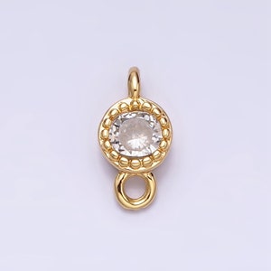 Op de afbeelding: Gouden hanger met een heldere ronde kristal omgeven door een parelrand. De hanger heeft een lus aan de onderkant om aan een ketting of koord te bevestigen.