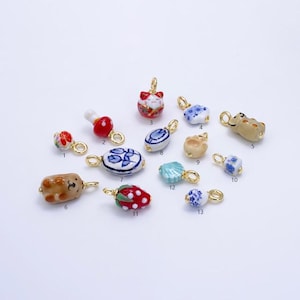 May include: Assortment of 13 ceramic charms with gold accents. The charms feature various designs, including a cat, a mushroom, a flower, a seashell, a strawberry, and a bear. The charms are perfect for adding a touch of whimsy to jewelry or other crafts.