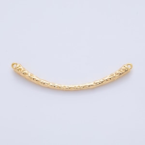 May include: A gold-colored, curved bar with a textured surface. The bar has small loops at each end, suggesting it is a jewelry component or decorative element. The overall design is simple yet elegant.