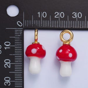 May include: Two red and white glass mushroom charms with gold jump rings. The charms are approximately 1 inch in size.