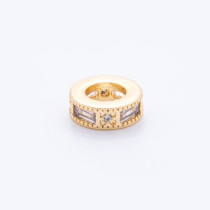 May include: A gold-colored spacer bead with a cylindrical shape. The bead features rectangular and round clear crystal accents. The bead is designed with a central hole for stringing and is suitable for jewelry making.