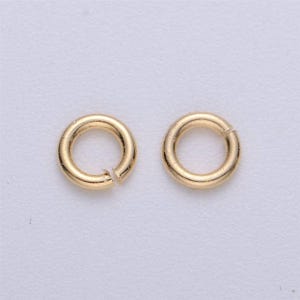 May include: Two gold jump rings, each with a circular shape and a small gap in the ring.