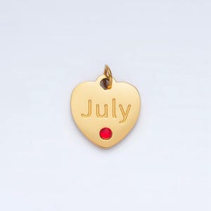 May include: Gold heart-shaped charm with the word "July" engraved on it. A small red gemstone is set in the center of the charm.