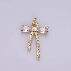 May include: A gold-toned pendant shaped like a bow, featuring two pear-shaped clear stones on the top loops and small round clear stones pavé-set along the two dangling tails and the center knot, complete with a small circular jump ring at the top.