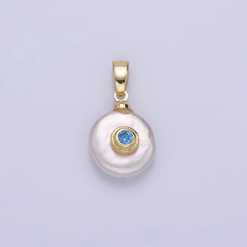 May include: A gold pendant featuring a white pearl with a blue gemstone set in a gold bezel.