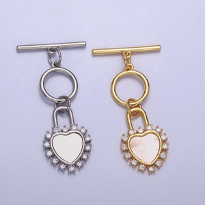 May include: Two silver and gold heart-shaped lock charms with clear crystal accents. Each charm is attached to a silver or gold toggle clasp.