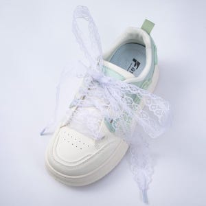 May include: A white and light green sneaker with white lace ribbon shoelaces. The shoe has a thick sole and a light green accent on the heel. The laces are tied in a bow.