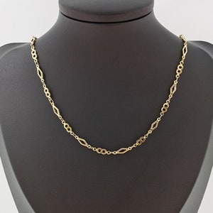 May include: A gold chain necklace with a delicate, intricate design. The chain features alternating oval and diamond-shaped links.