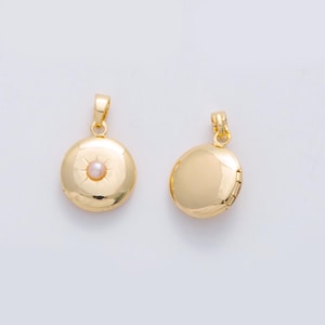Könnte beinhalten: Zwei goldfarbene, runde Medaillons mit einer kleinen Schlaufe oben für eine Kette. Ein Medaillon hat ein Sonnenstrahl-Design mit einer kleinen, hellrosa Perle in der Mitte. Das andere Medaillon ist schlicht.