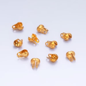 May include: A group of ten gold-coloured metal bead caps with a loop on each side. The bead caps are designed to be used as end caps for necklaces, bracelets, or other jewellery.