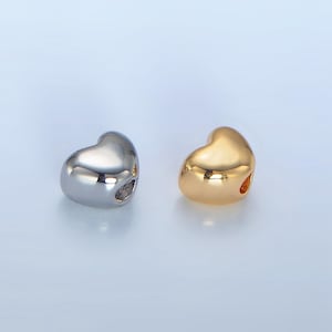 May include: Two heart-shaped charms, one silver and one gold, with a hole for threading onto a bracelet or necklace.