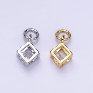 May include: Two square-shaped pendant charms with a clear crystal inside. The charm on the left is silver and the charm on the right is gold.