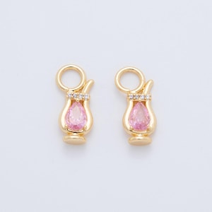 May include: Two gold-coloured cocktail-shaped charms with a pink teardrop-shaped gem in the centre. The charms have a loop at the top and are embellished with small clear stones. The charms are on a white background.