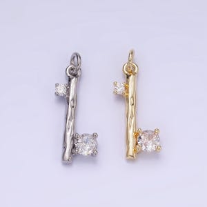 May include: Two silver and gold key charms with clear crystal accents. The charms are shaped like a twig with a small round crystal at the top and a larger round crystal at the bottom.