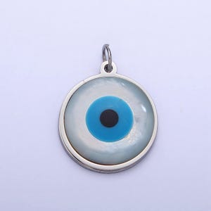 May include: A silver charm with a white and blue evil eye design. The eye is surrounded by a silver circle.