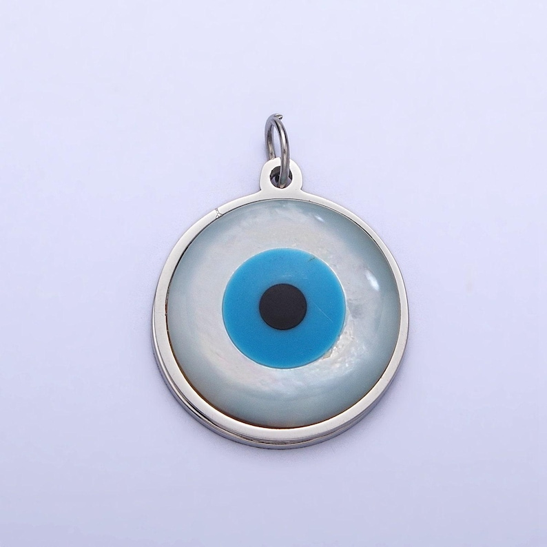 May include: A silver charm with a white and blue evil eye design. The eye is surrounded by a silver circle.