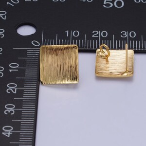 Könnte beinhalten: Zwei goldene quadratische Ohrringe mit gebürsteter Oberfläche. Die Ohrringe sind etwa 1 cm groß.